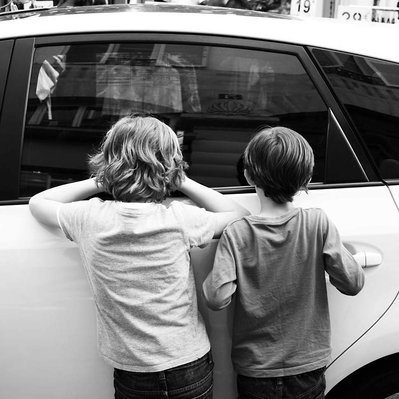 Black and white street photography of the french street photographer David Décamps representing two kids watching inside a car in Paris.