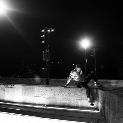 Black and white street photography of the french street photographer David Décamps representing a man kicking the air on a bridge in Paris during the night.