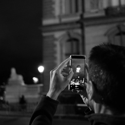 Black and white street photography of the french street photographer David Décamps representing a man taking a picture of the Olympic flame in Paris.