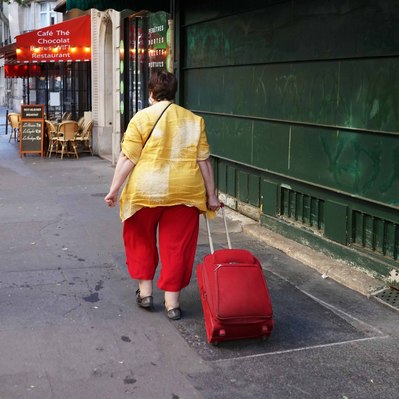 Street photography in colors of the french street photographer David Décamps representing a woman with a red pants and suitcase in Paris.