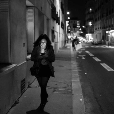 Black and white street photography of the french street photographer David Décamps representing a woman alone walking with the light of her phone in her face in Paris.