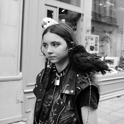 Black and white street photography of the french street photographer David Décamps representing a girl with two birds on her shoulders in Paris.