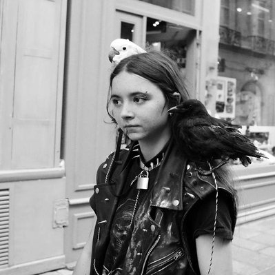 Black and white street photography of the french street photographer David Décamps representing a girl with two birds on her shoulders in Paris.