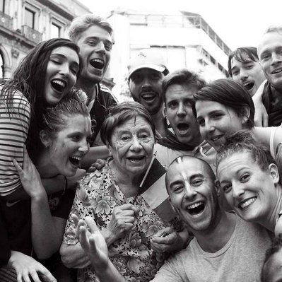 Black and white street photography of the french street photographer David Décamps representing a crowd of young people celebrating around an old woman in Paris.
