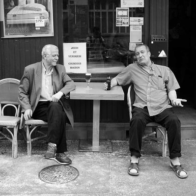 Black and white street photography of the french street photographer David Décamps representing two best friends drinking in a tiny terrace in Paris.
