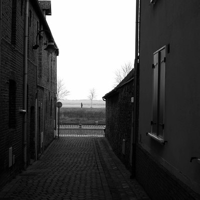 Black and white street photography of the french street photographer David Décamps representing a tiny figure in the middle of the street in Saint-Valery-sur-Somme, France.
