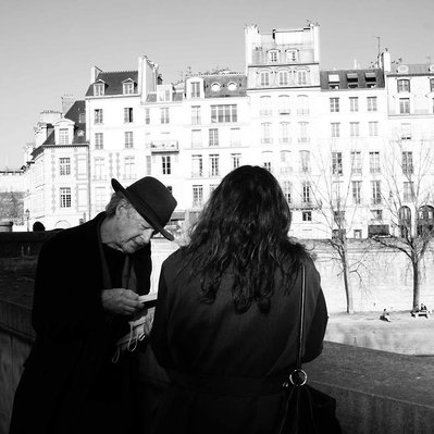 Black and white street photography of the french street photographer David Décamps representing a man reading a book to a woman on a bridge in Paris.