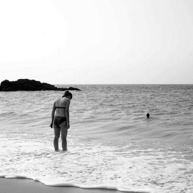 Black and white street photography of the french street photographer David Décamps representing a young girl with her feet in the water close to the ocean.