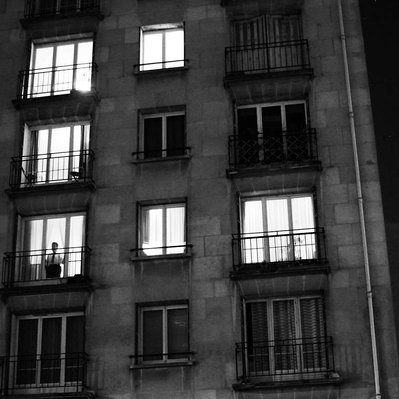Black and white street photography of the french street photographer David Décamps representing a man alone at his window during the night in a building in Paris.