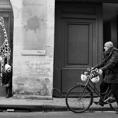 Black and white street photography of the french street photographer David Décamps representing a little girl hide behind a wall scary her father in Paris.