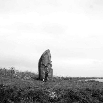 Black and white street photography of the french street photographer David Décamps representing a kid running close to a big rock.