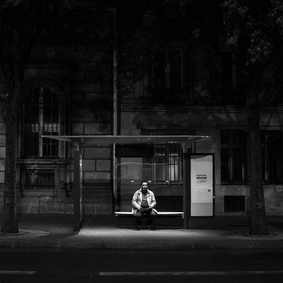 Black and white street photography of the french street photographer David Décamps representing a man alone at the bus station in the night in Paris.
