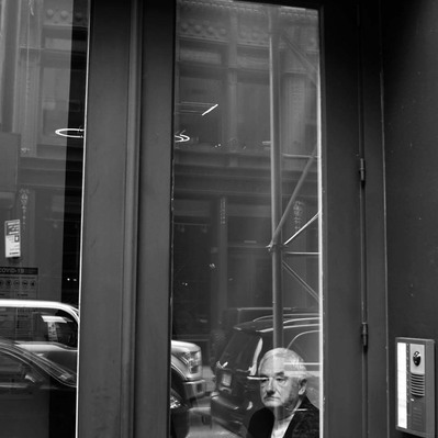 Black and white street photography of the french street photographer David Décamps representing a doorman sitting and waiting at a door in New York City, USA.
