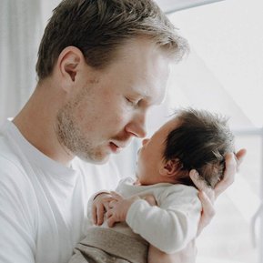 Papa und neugeborenes Baby kuscheln miteinander.