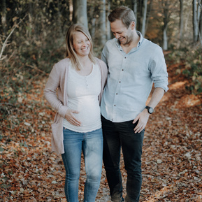 Schwangere Frau mit werdenden Papa gehen durch den herbstlichen Wald.