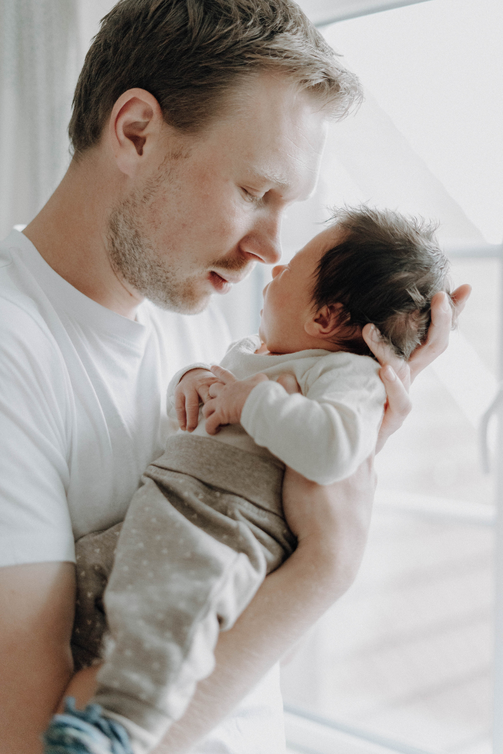 Junger Papa hält sein Baby in den Armen und schmust mit ihm.