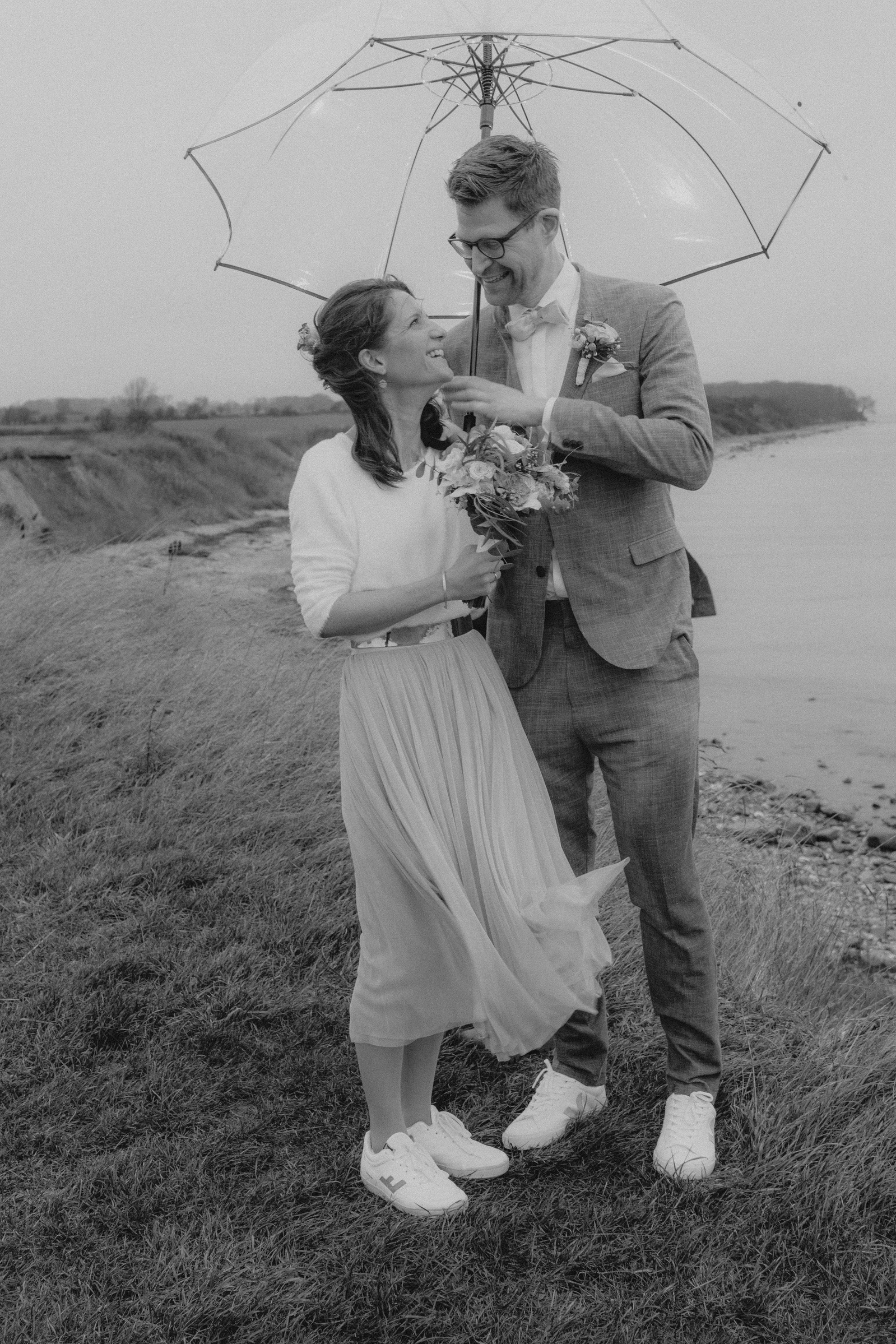 Brautpaar unterm durchsichtigen Regenschirm an der Steilküste.