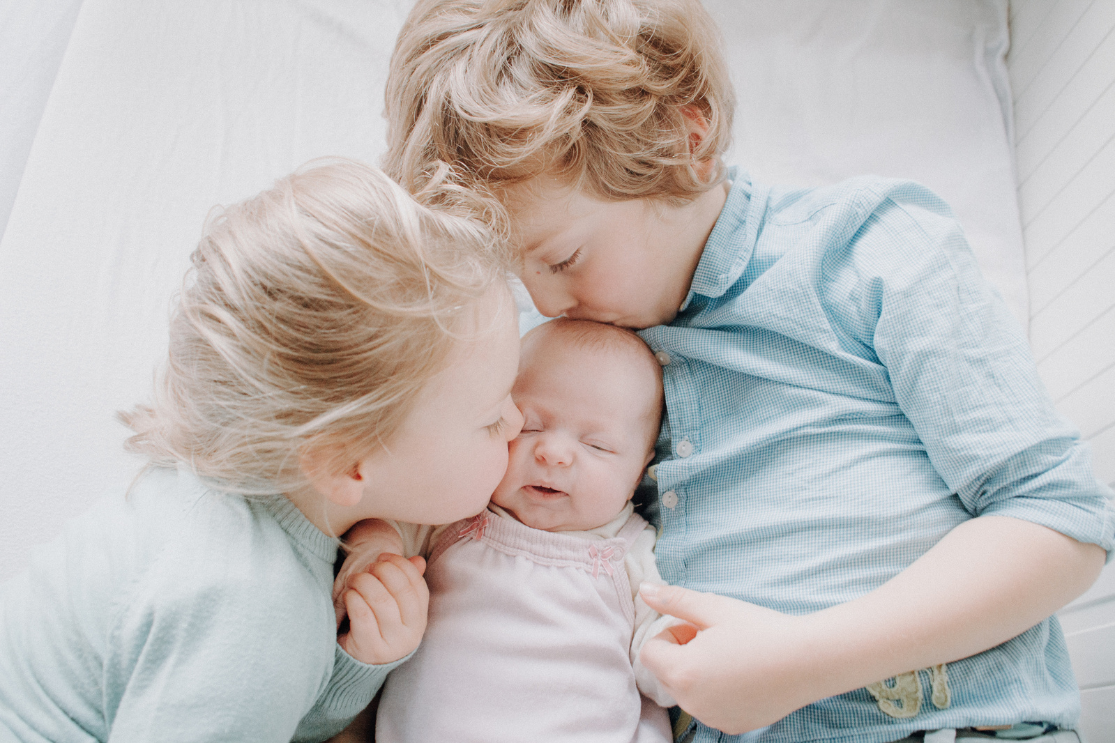Geschwisterfoto in Kiel und Umgebung. Junge und Mädchen küssen Baby.