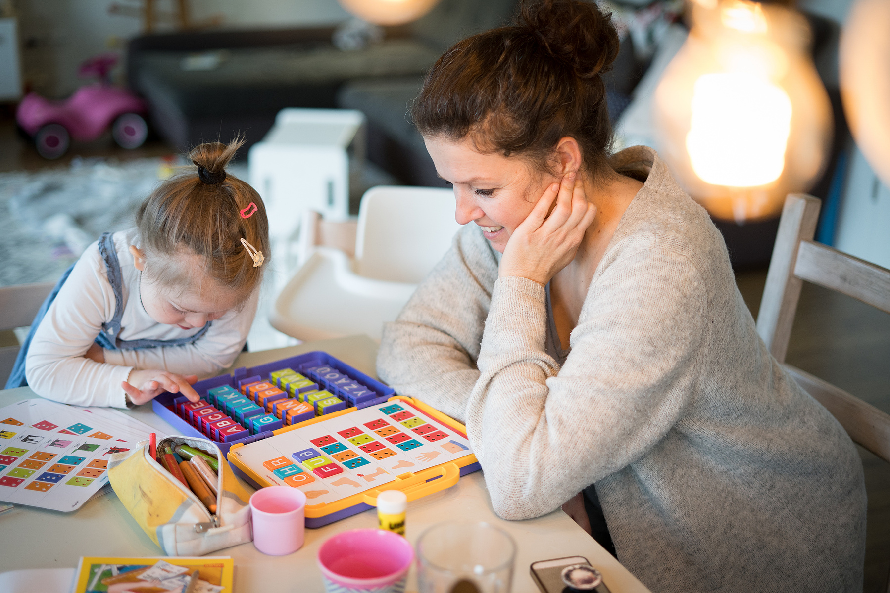 Mutter und Mädchen mit DownSyndrom sitzen am Tisch und lernen.