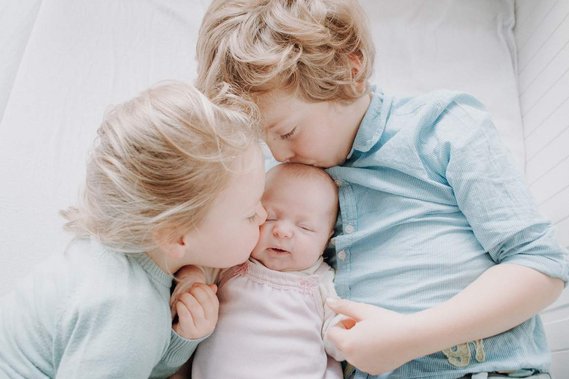 Geschwister küssen neugeborenes Baby.