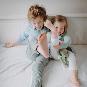 Geschwister Kinder strecken ihre nackten Füße in die Kamera und lachen.