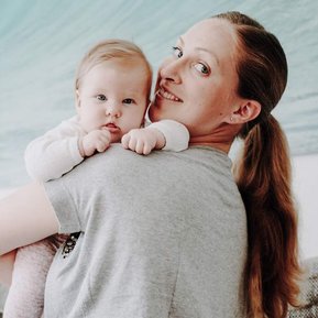 Junge Mama trägt ihr Baby über der Schulter.