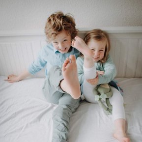 Geschwister Kinder strecken ihre nackten Füße in die Kamera und lachen.