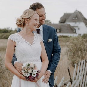 Brautpaar am Hochzeitstag steht vor Reetdachhaus an der Hohwachter Bucht.
