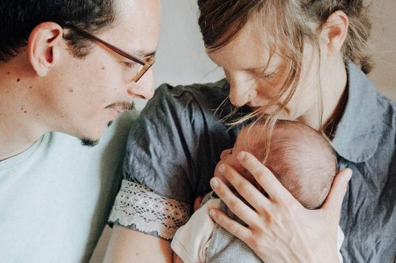 Junger Vater und Mutter halten Neugeborenes und kuscheln.