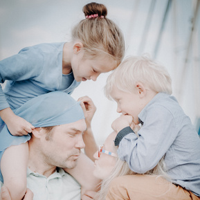Familienportrait im Segelyachthafen Schilksee bei Kiel von Mutter und Vater, die Sohn und Tochter auf den Schultern haben und sich küssen.