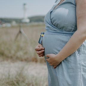 Nahaufnahme vom Babybauch am Strand mit Leuchtturm im Hintergrund.