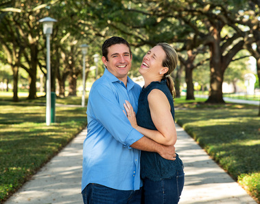 A couple laughs while standing on a path beneath trees
