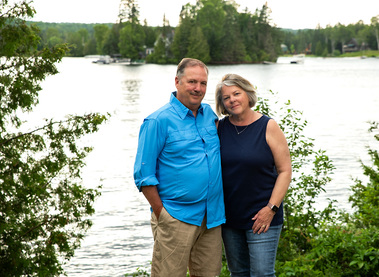 An older couple stands on their lawn by the water in Vermont