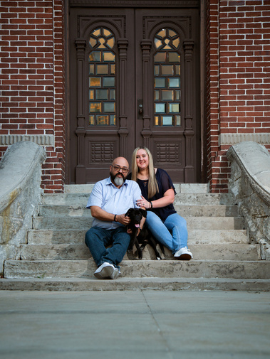 A married couple sits on the steps of a building with their puppy