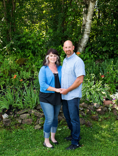 A married couple stand together outside on their front lawn in Vermont