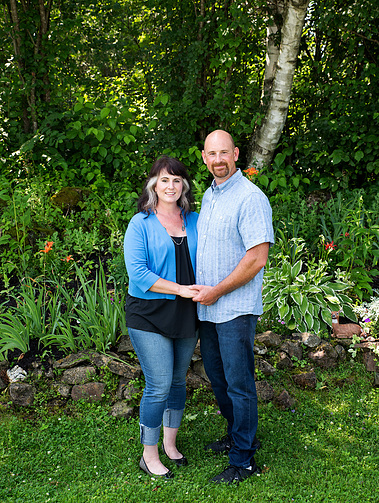A married couple stand together outside on their front lawn in Vermont