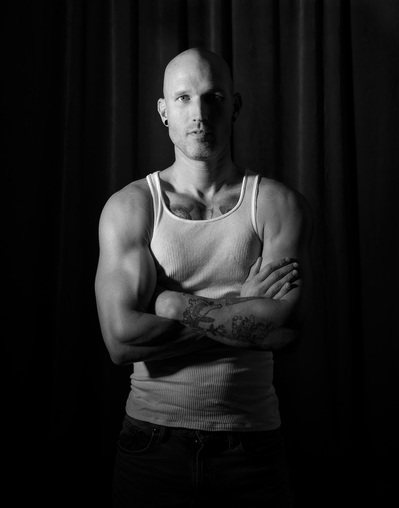 A man stand  with his arms crossed for a black and white portrait by Dark Light Portrait Studios 