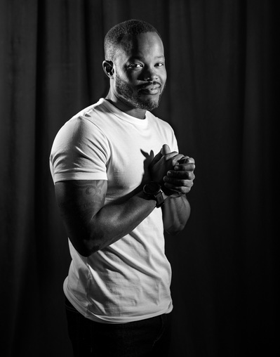 A man in a white t-shirt poses for a black and white portrait during The Man Project by Dark Light Portrait Studios. 