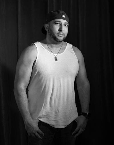 A hispanic man poses for a black and white portrait for the Man Project by Dark Light Portrait Studios
