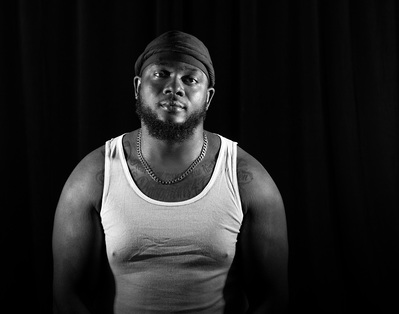 A man with a beard poses in a white tank top for a black and white portrait by Dark Light Portrait Studios