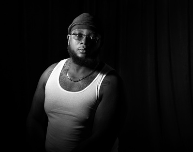 A man wearing glasses poses for a low key black and white portrait by Dark Light Portrait Studios