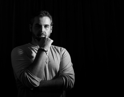 A man poses on a black background for a black and white photo project for Dark Light Portrait Studios
