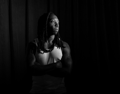 An African American man with dreads poses for a low key portrait by Dark Light Portrait Studios