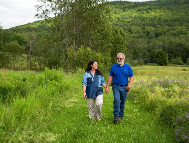 A married couple walks hand in hand in a field in Vermont