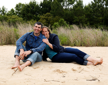 A married couple sit in the sand at the beach 