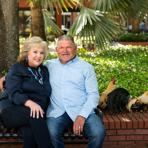 A married couple site on a bench in Ybor City, FL with roosters behind them