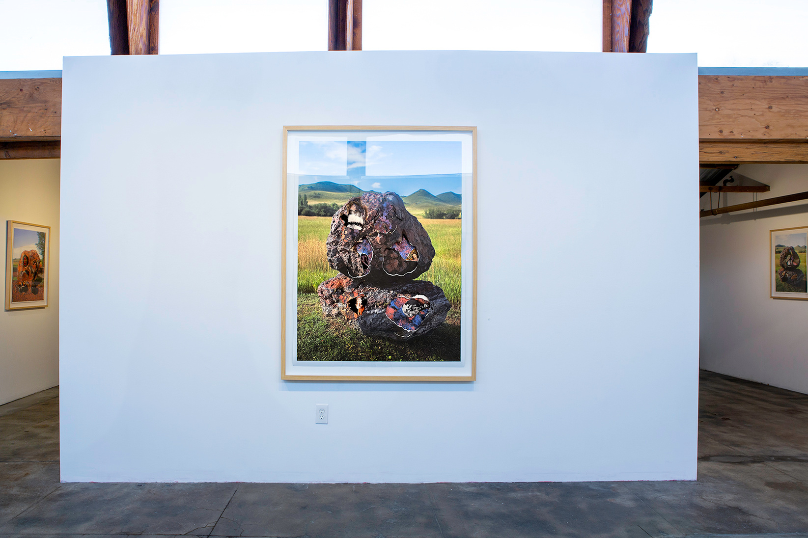 Landscape shot in the wide open spaces of Wyoming featuring 2 large purple and black rocks piled on top of each other. The photograph is then printed multiple times and layered on top of each other with holes torn and burned into them.