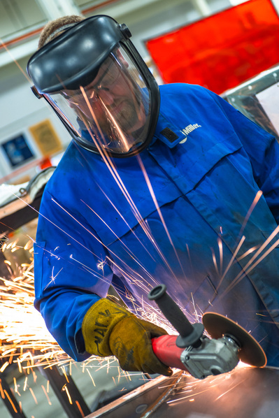 A metal worker grinding down a seam on a metal construction, surrounded by sparks