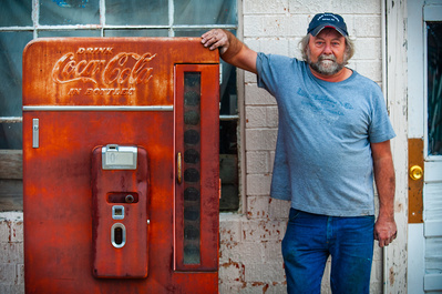 A male shopkeeper posing next to an old red Coca-Cola machine in Arizona