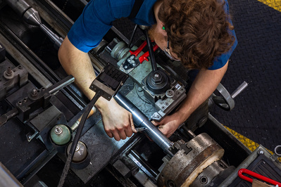 Young technician machining an industrial part on a lathe for the manufacture of miter machines